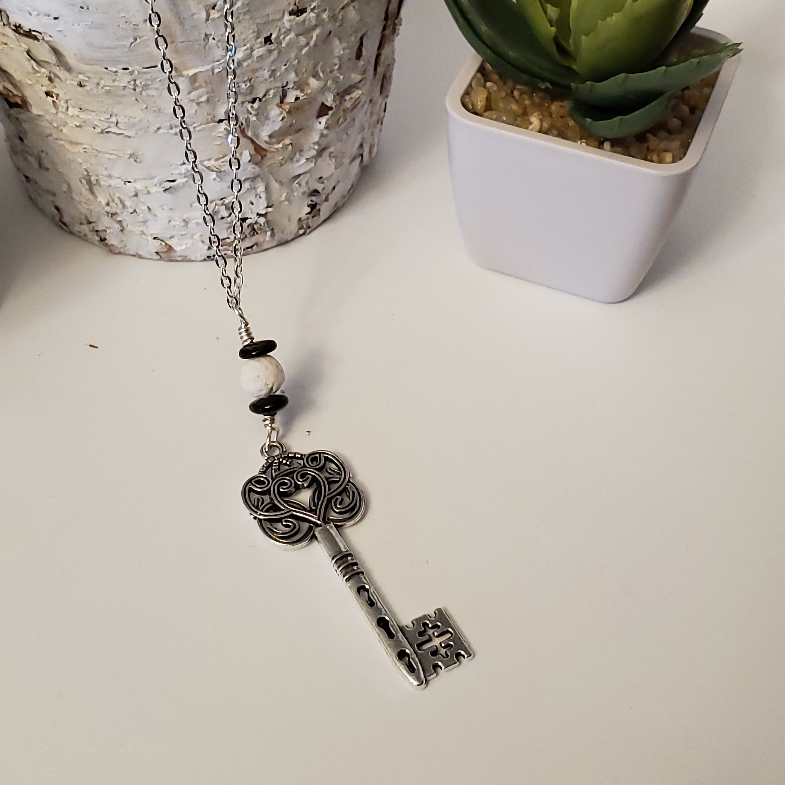 Long chain necklace with key-shaped charm and a White Lava Bead