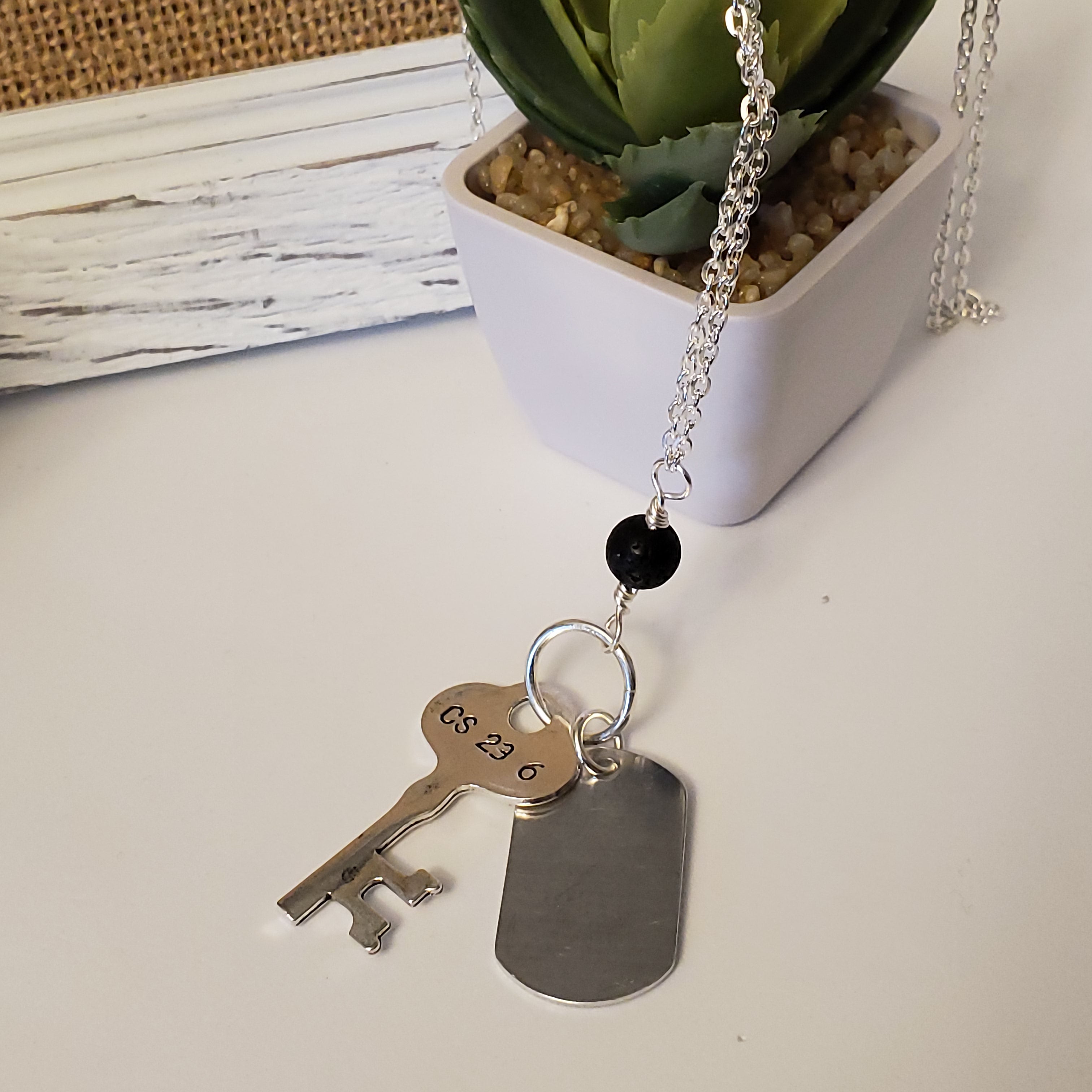 Long chain necklace with key-shaped charm, dog tag and black lava bead